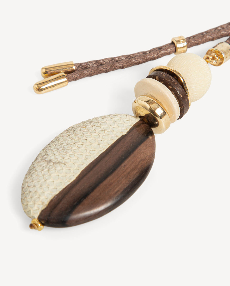 Detalle del collar Luxue de Emolo con colgante ovalado marrón y beige, discos apilados y cuenta redonda clara