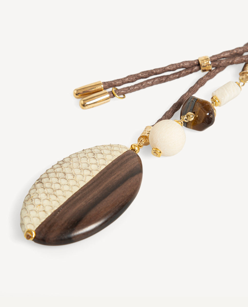 Detalle del collar Luxue ojo de tigre de Emolo con colgante ovalado marrón y beige, cuentas claras y cordón trenzado