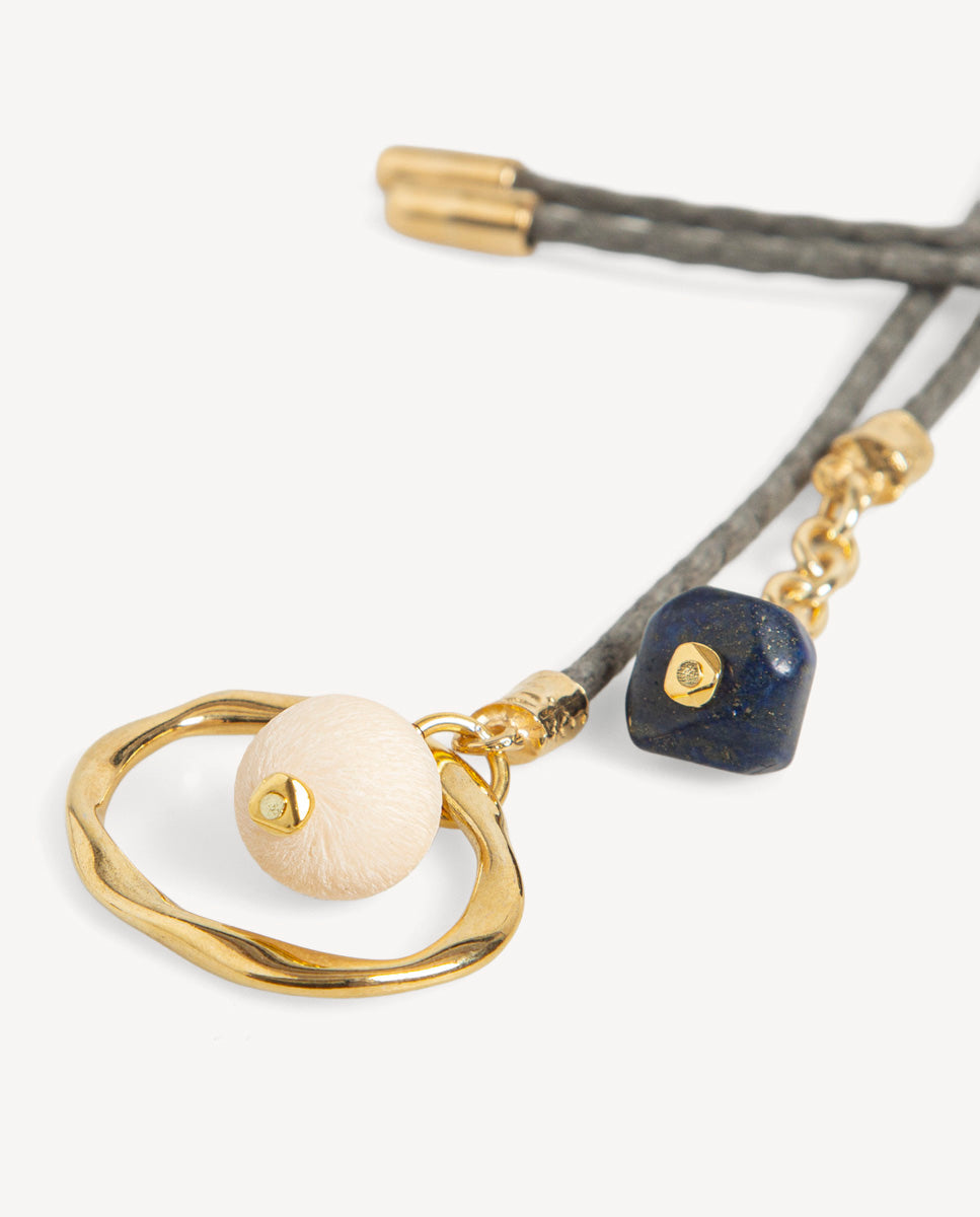 Detalle del collar Nimbo Monsul gris de Emolo con aro dorado irregular, cuenta redonda blanca y cuenta azul oscuro