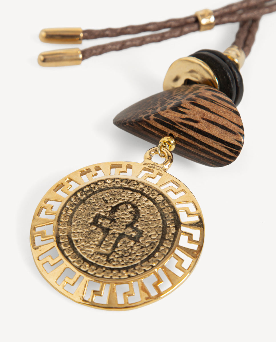 Detalle del collar Monsul Met de Emolo con medallón dorado de grecas caladas y cuenta triangular marrón veteada