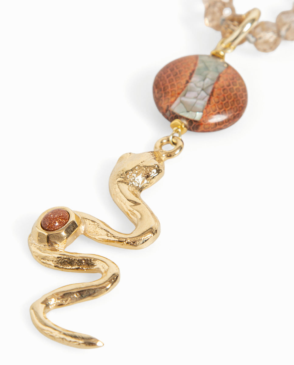 Detalle del collar Odri Ambera translúcido de Emolo: serpiente dorada y pieza redonda marrón con dibujo de escamas