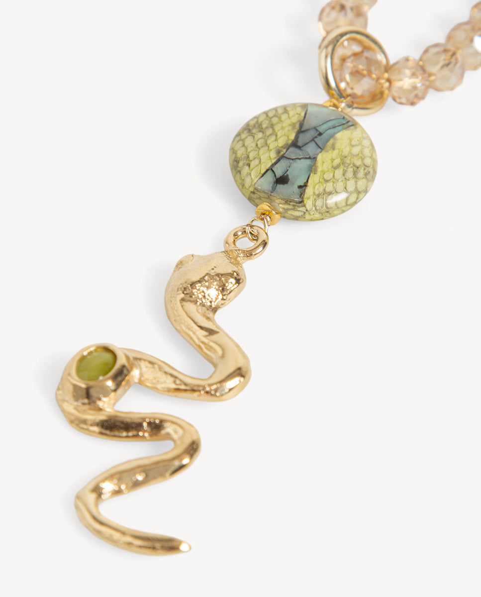 Detalle del collar Odri Ambera dorado de Emolo: serpiente dorada con piedra verde y pieza redonda con dibujo de escamas