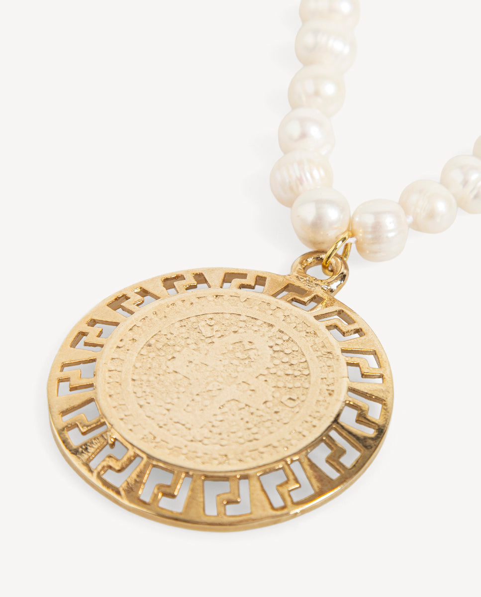 Detalle del collar Perlas Met de Emolo con perlas blancas y medallón circular dorado con borde de grecas caladas