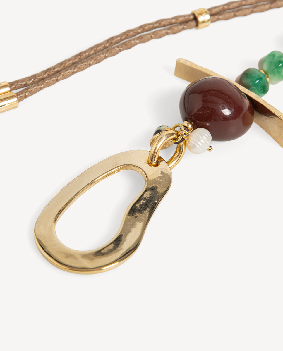 Detalle del collar Hanner marrón de Emolo con colgante dorado de gota calada, cuenta marrón y pequeña cuenta blanca