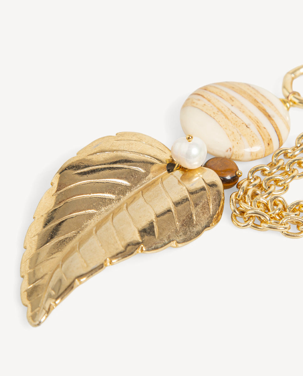 Detalle del collar Tessoa beige de Emolo con hoja dorada, cuenta ovalada de rayas beige y blancas y perla blanca