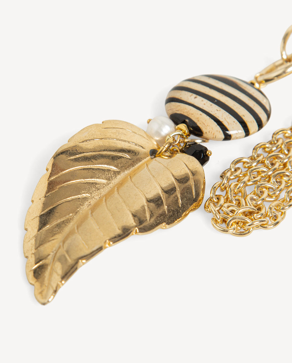 Detalle del collar Tessoa rayada de Emolo con hoja dorada, cuenta ovalada de rayas negras y beige y perla blanca
