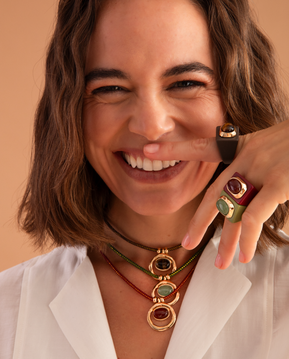Modelo con anillos grandes y tres collares cortos de Émolo con cordones de colores y colgantes dorados