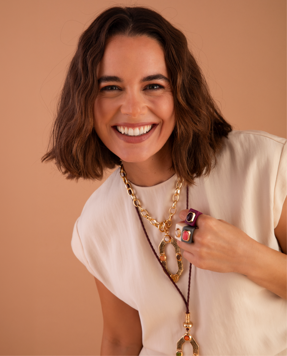Modelo con collares de Émolo de cadena dorada y cordón marrón, colgantes geométricos y anillos de colores
