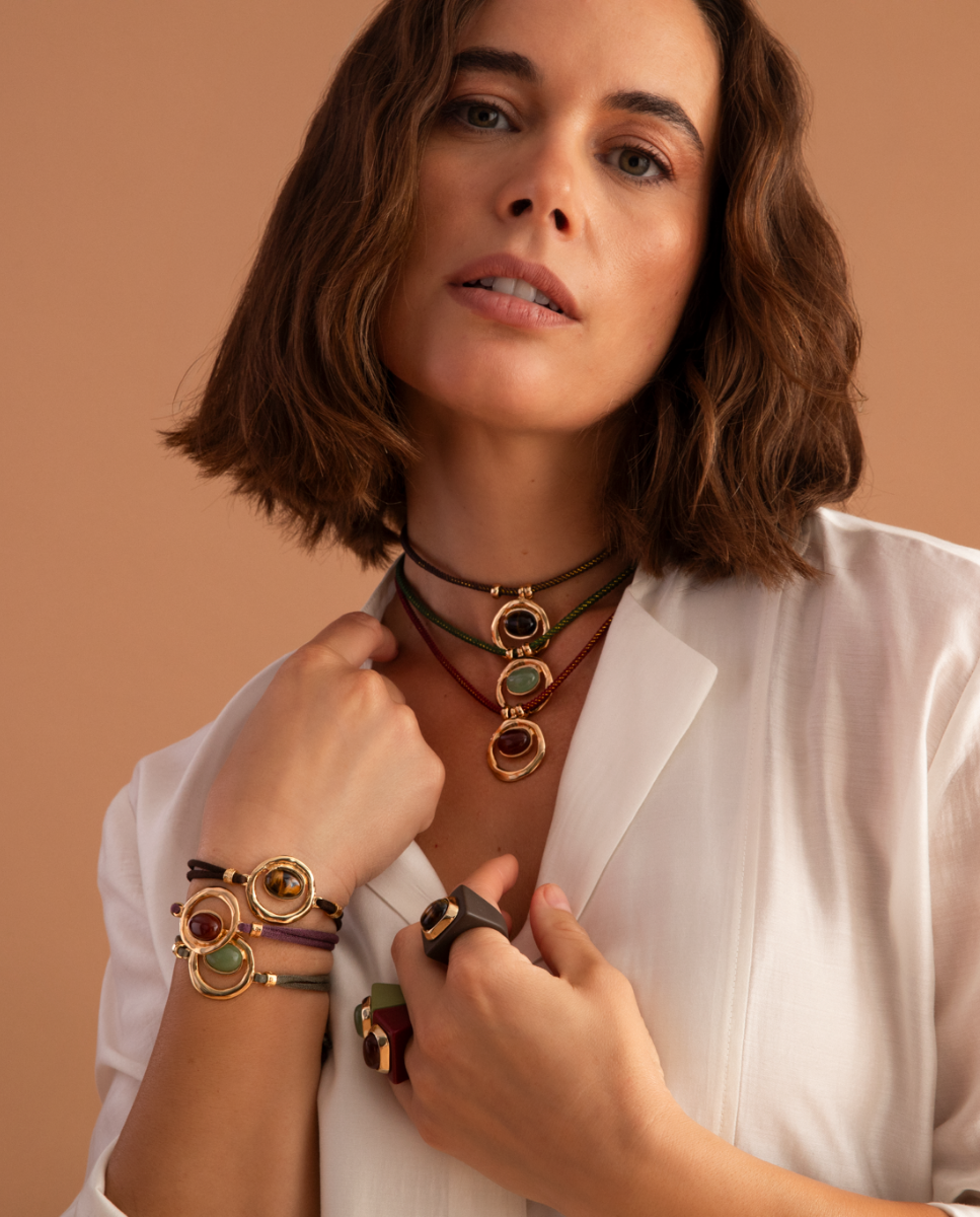 Model wearing Émolo cord necklaces and bracelets with gold-tone oval pendants and colourful stones