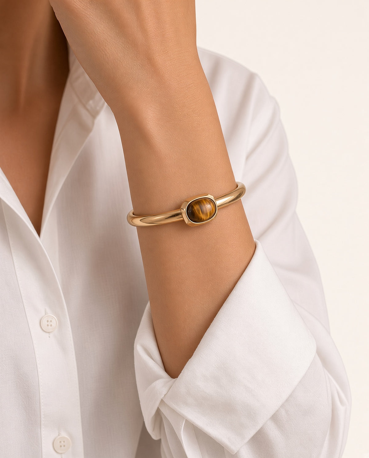 Modelo con el brazalete Luvo de Emolo en dorado con ojo de tigre, sobre camisa blanca