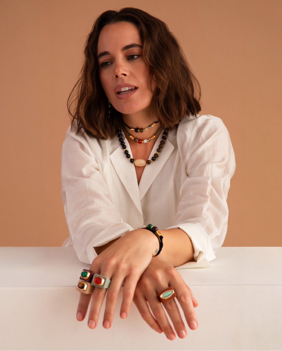 Modelo con camisa blanca, anillos de colores, collares y pulsera de Émolo