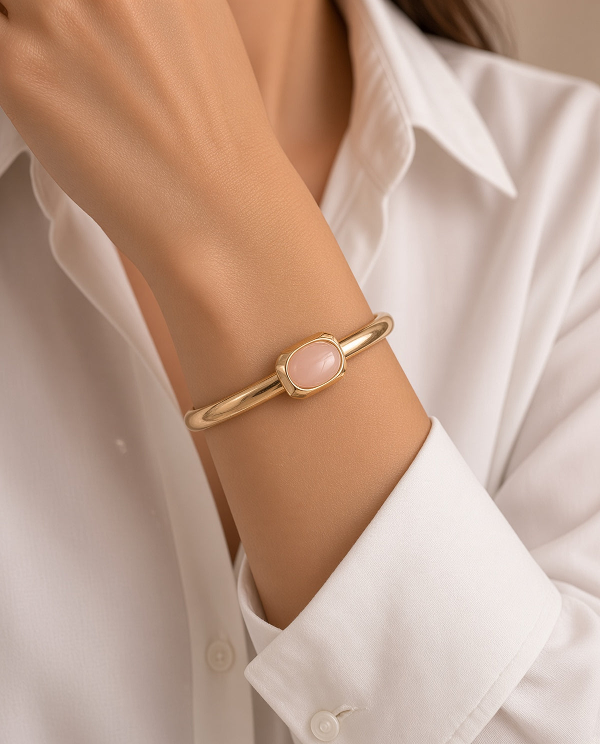 Modelo con el brazalete Luvo de Emolo en dorado con cuarzo rosa, sobre camisa blanca