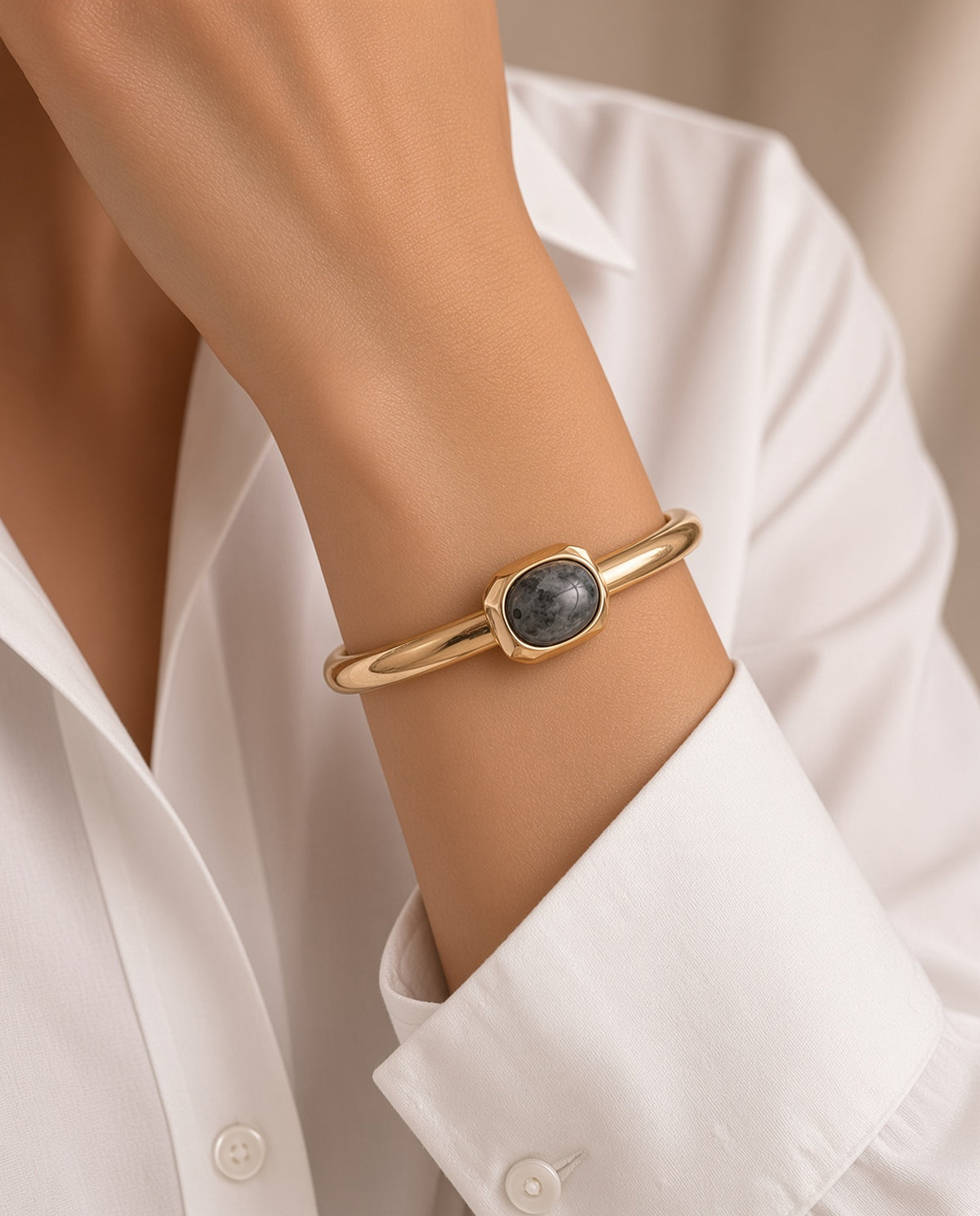 Modelo con el brazalete Luvo de Emolo en dorado con labradorita gris, sobre camisa blanca