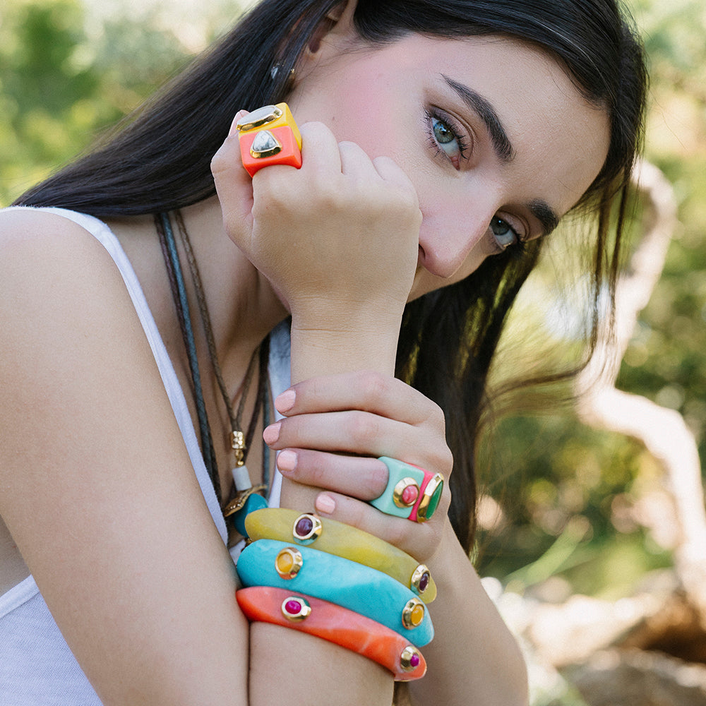 Modelo con anillos anchos Emolo naranja flúor, amarillo y mint y pulseras grandes de colores con piedras en marcos dorados