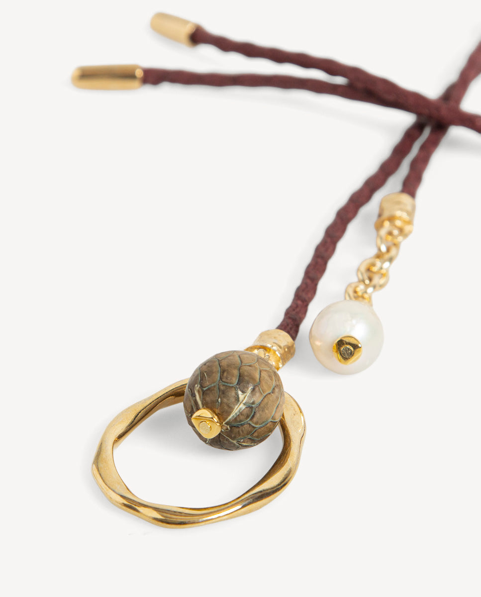 Detalle del collar Nimbo Monsul burdeos de Emolo con aro dorado irregular, cuenta verde con vetas y cuenta blanca