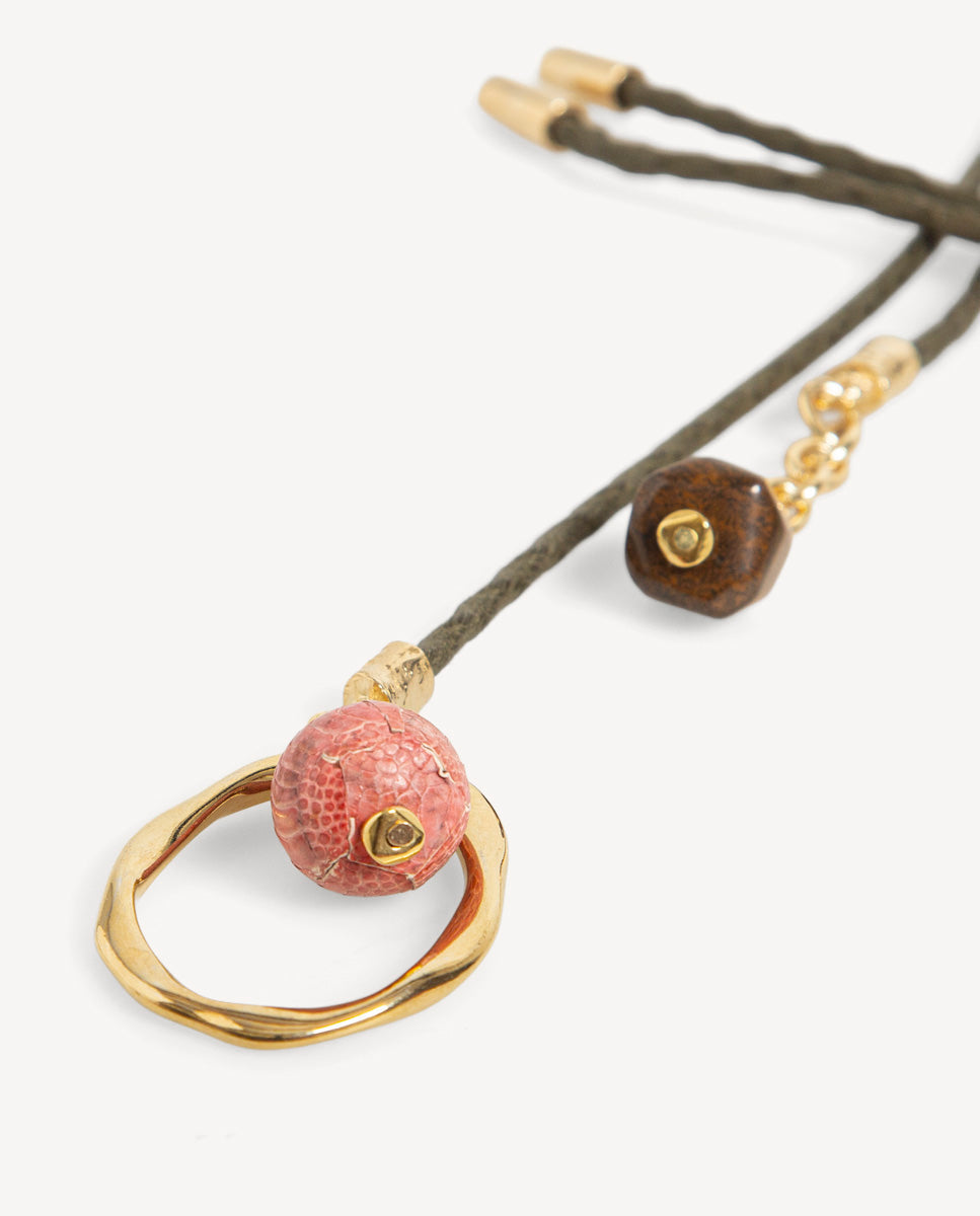Detalle del collar Nimbo Monsul kaki de Emolo con aro dorado irregular, cuenta redonda rosada y cuenta marrón